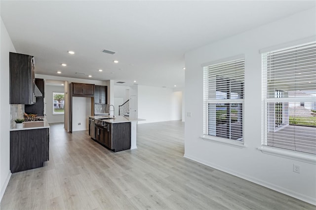 kitchen with dark brown cabinetry, a sink, visible vents, open floor plan, and light wood finished floors