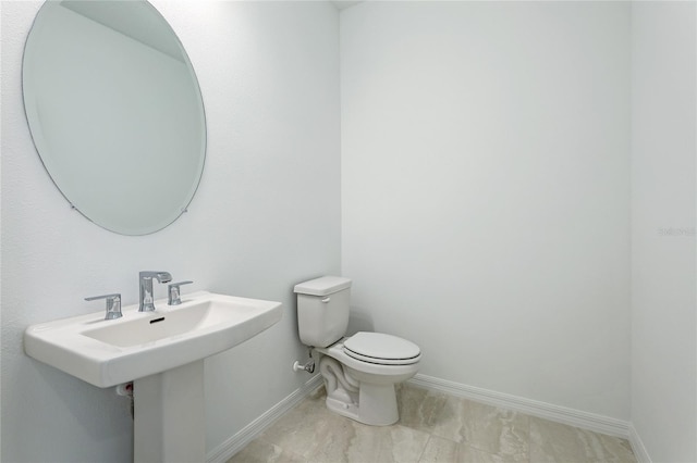 half bath with toilet, baseboards, and a sink