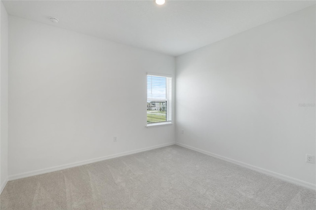 spare room featuring light carpet and baseboards