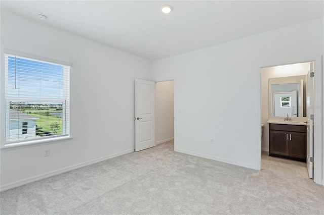 unfurnished bedroom featuring light carpet, a sink, connected bathroom, and baseboards