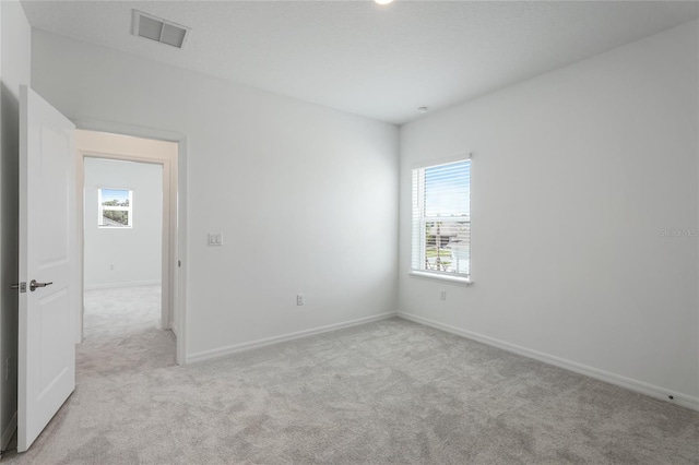 spare room featuring light colored carpet, visible vents, and baseboards