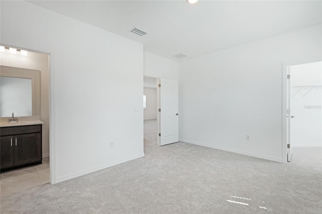 unfurnished bedroom with visible vents, a spacious closet, light carpet, a sink, and baseboards