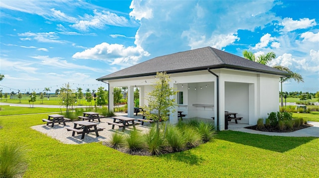 rear view of property featuring roof with shingles, stucco siding, a yard, and a patio