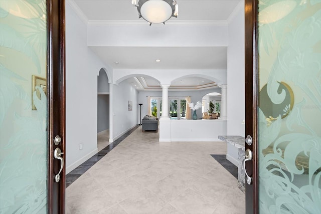 entrance foyer with decorative columns, a raised ceiling, and crown molding