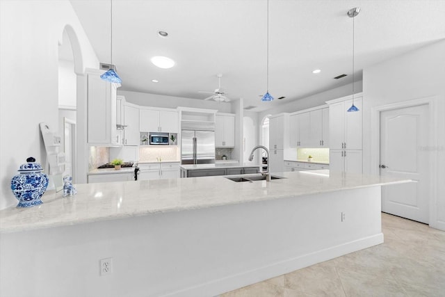 kitchen featuring light stone counters, sink, built in appliances, decorative light fixtures, and white cabinetry