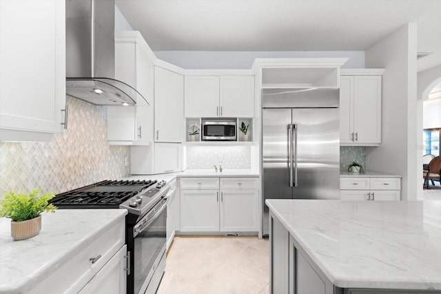 kitchen with white cabinets, built in appliances, light stone counters, and wall chimney range hood