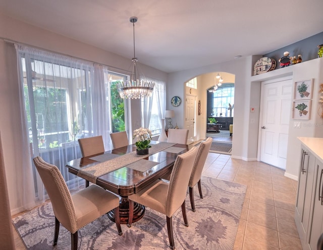 dining space with arched walkways, a notable chandelier, baseboards, and light tile patterned floors