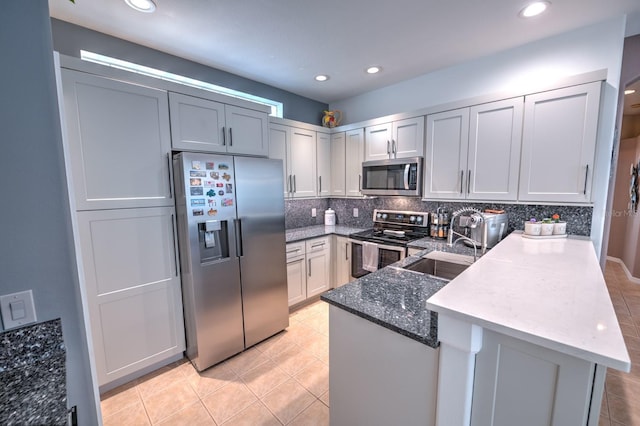 kitchen featuring tasteful backsplash, appliances with stainless steel finishes, a sink, dark stone counters, and a peninsula