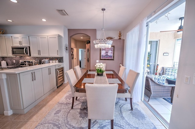 dining area featuring light tile patterned floors, beverage cooler, visible vents, arched walkways, and an inviting chandelier