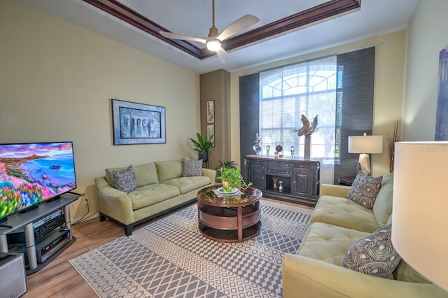 living room featuring wood finished floors, a raised ceiling, a ceiling fan, and crown molding