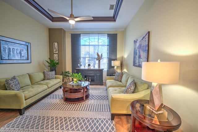 living room with a tray ceiling, wood finished floors, visible vents, and crown molding