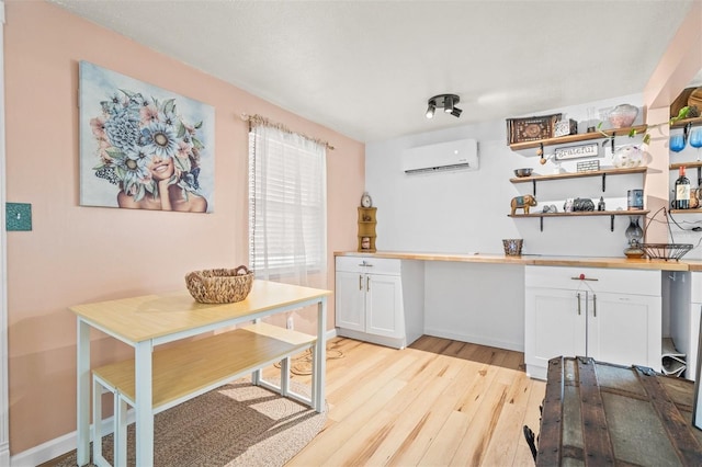 kitchen featuring light hardwood / wood-style flooring, white cabinetry, and a wall mounted air conditioner