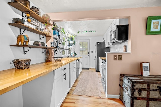 kitchen featuring light wood-type flooring, stainless steel appliances, white cabinetry, wooden counters, and a textured ceiling