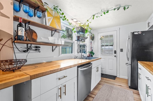 kitchen with light wood-type flooring, appliances with stainless steel finishes, a textured ceiling, and butcher block countertops