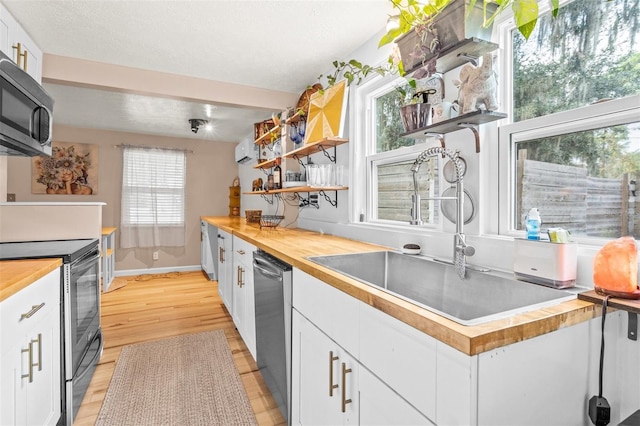 kitchen with a wealth of natural light, stainless steel appliances, white cabinetry, and wood counters