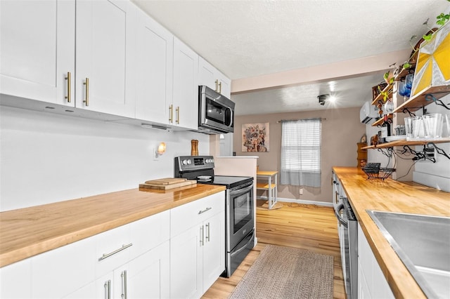 kitchen featuring white cabinets, wood counters, light wood-type flooring, appliances with stainless steel finishes, and sink