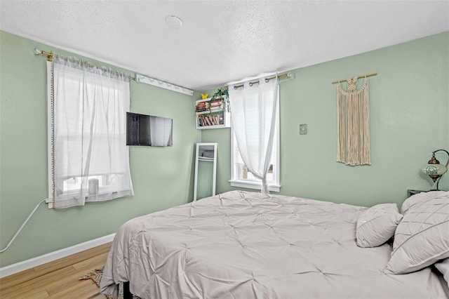 bedroom featuring light wood-type flooring, multiple windows, and a textured ceiling