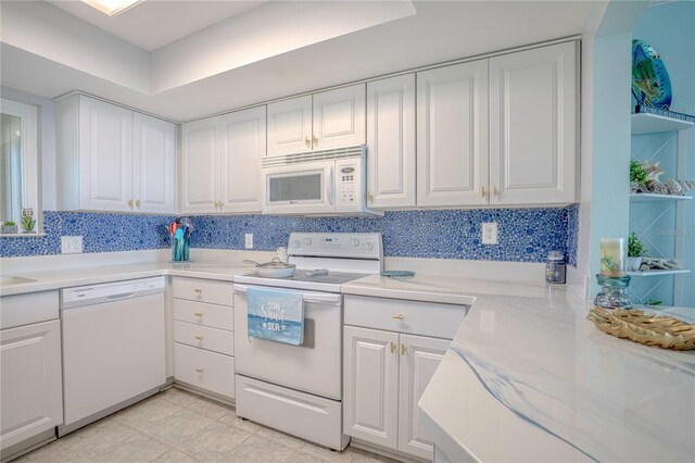 kitchen featuring light tile patterned flooring, backsplash, white appliances, a tray ceiling, and white cabinetry