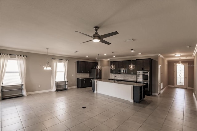 kitchen with backsplash, light tile patterned floors, stainless steel appliances, crown molding, and a center island with sink