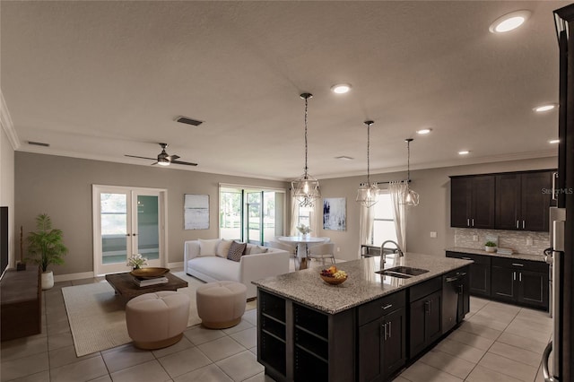 kitchen featuring sink, ornamental molding, light stone countertops, and a center island with sink