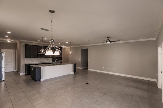 kitchen with a kitchen island with sink, pendant lighting, crown molding, and refrigerator