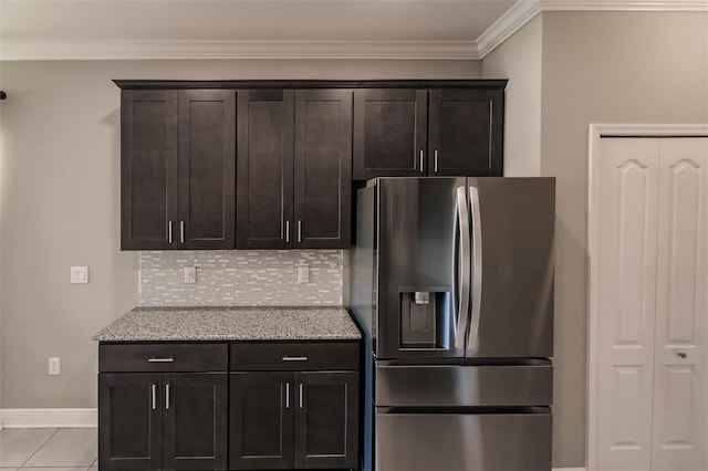 kitchen with stainless steel refrigerator with ice dispenser, backsplash, light stone counters, crown molding, and dark brown cabinets