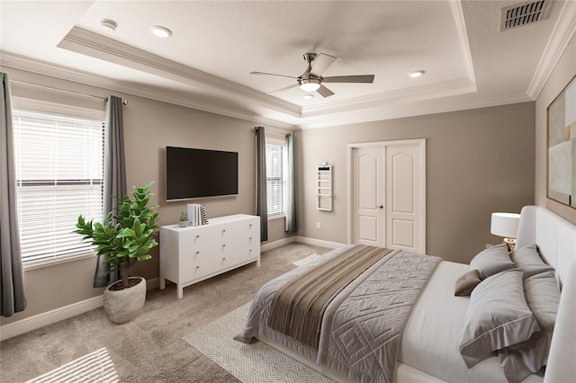 bedroom with ornamental molding, light colored carpet, ceiling fan, a tray ceiling, and a textured ceiling