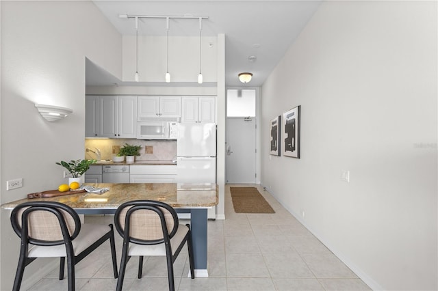 kitchen featuring light stone counters, kitchen peninsula, white appliances, a breakfast bar, and white cabinets