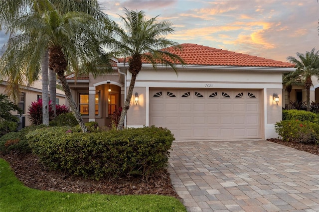 mediterranean / spanish-style home featuring a tiled roof, decorative driveway, a garage, and stucco siding