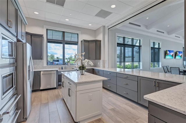 kitchen with gray cabinets, light stone countertops, decorative backsplash, appliances with stainless steel finishes, and light hardwood / wood-style floors