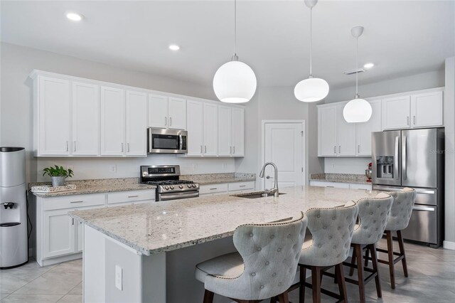 kitchen with a center island with sink, stainless steel appliances, sink, white cabinetry, and light tile patterned flooring