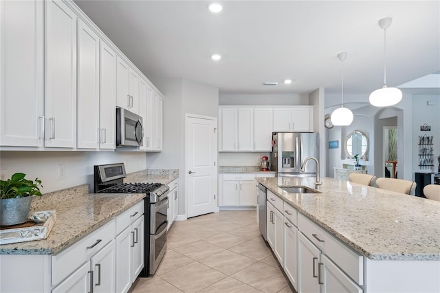 kitchen with a kitchen island with sink, white cabinetry, light tile patterned floors, stainless steel appliances, and hanging light fixtures