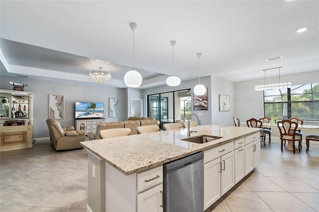 kitchen with a notable chandelier, white cabinetry, a center island with sink, a tray ceiling, and stainless steel dishwasher