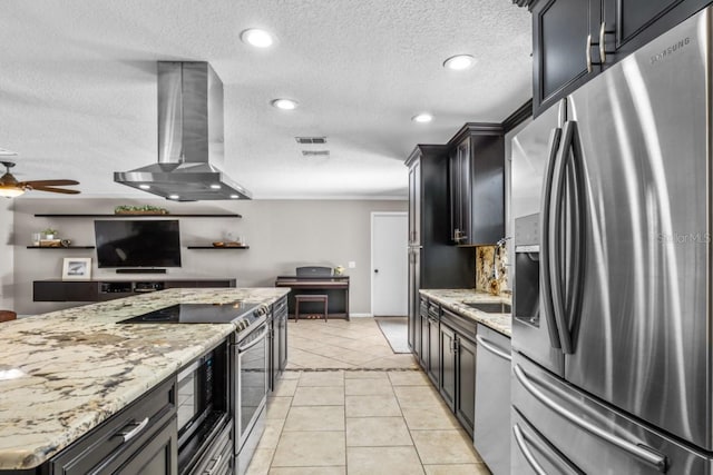 kitchen with stainless steel appliances, wall chimney range hood, light tile patterned floors, and light stone counters