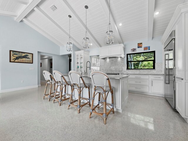 kitchen with beamed ceiling, backsplash, a kitchen island with sink, hanging light fixtures, and white cabinetry