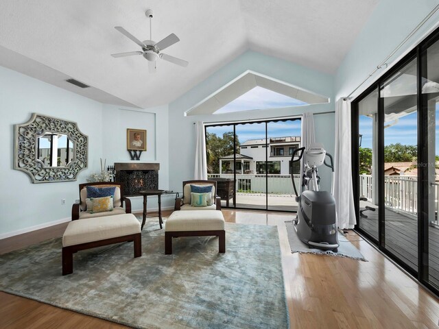 living area featuring lofted ceiling, ceiling fan, wood-type flooring, and a fireplace