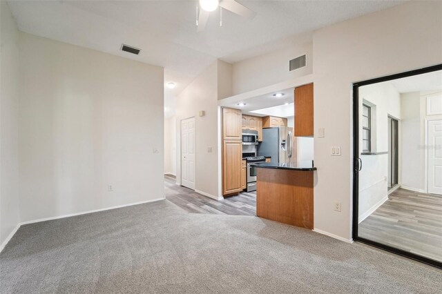 kitchen featuring light carpet, stainless steel appliances, kitchen peninsula, ceiling fan, and vaulted ceiling