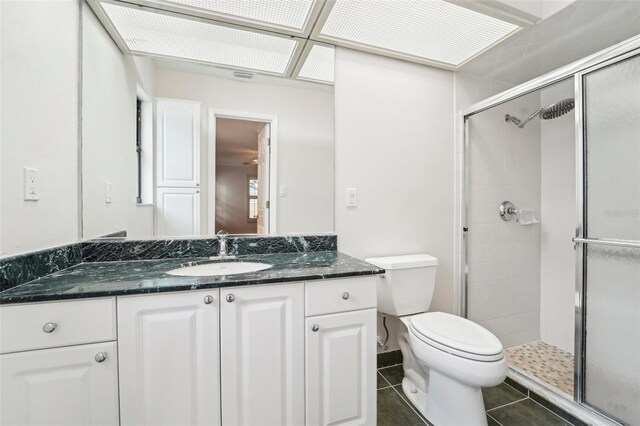 bathroom with a shower with door, vanity, toilet, and tile patterned floors