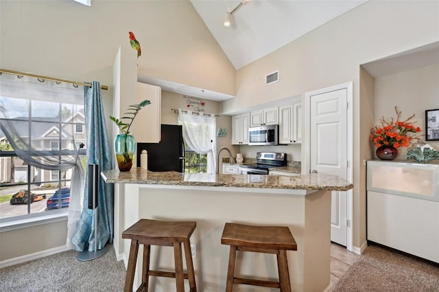 kitchen featuring kitchen peninsula, light stone countertops, appliances with stainless steel finishes, and a breakfast bar area