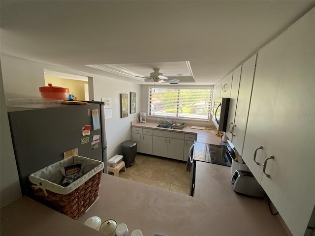 kitchen featuring white cabinets, stainless steel appliances, ceiling fan, a tray ceiling, and light tile patterned flooring