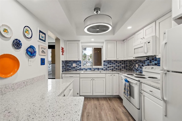 kitchen with white cabinetry, white appliances, sink, decorative backsplash, and light hardwood / wood-style floors