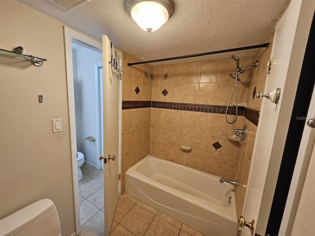 bathroom with tile patterned flooring, toilet, a textured ceiling, and tiled shower / bath