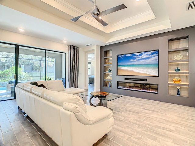 cinema room with ornamental molding, built in features, ceiling fan, a tray ceiling, and hardwood / wood-style flooring