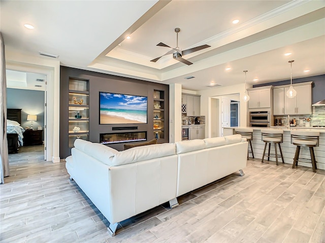 living room featuring beverage cooler, a tray ceiling, built in features, ceiling fan, and light wood-type flooring