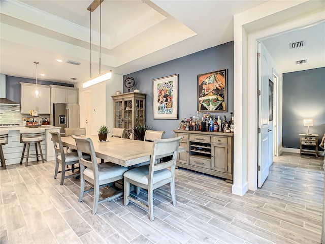 dining space featuring a raised ceiling, bar, and light hardwood / wood-style floors