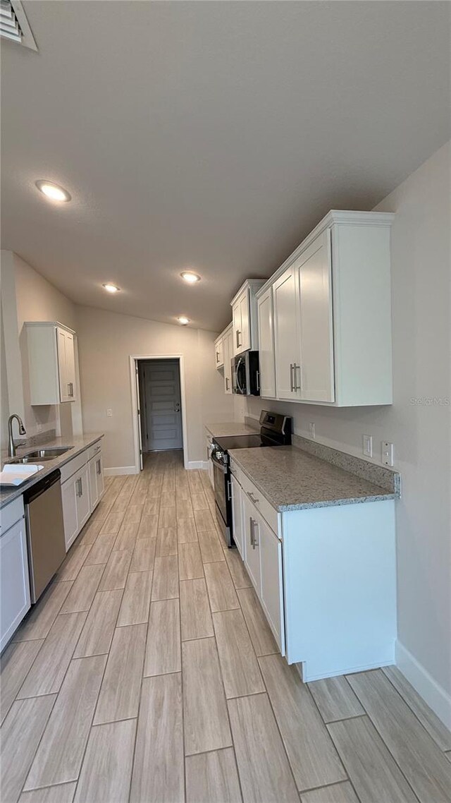 kitchen with white cabinets, sink, vaulted ceiling, light stone countertops, and appliances with stainless steel finishes