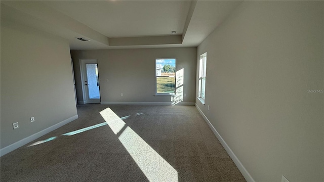 spare room with visible vents, a tray ceiling, baseboards, and carpet flooring