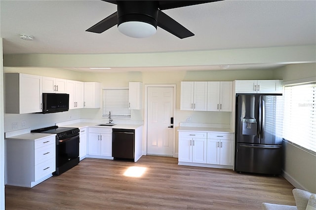 kitchen with black appliances, sink, light wood-type flooring, ceiling fan, and white cabinets