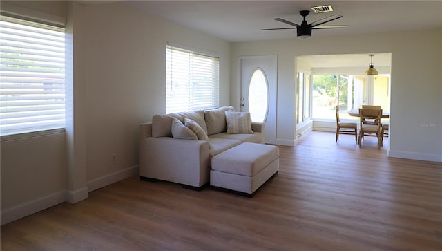 living area featuring a ceiling fan, wood finished floors, visible vents, and baseboards