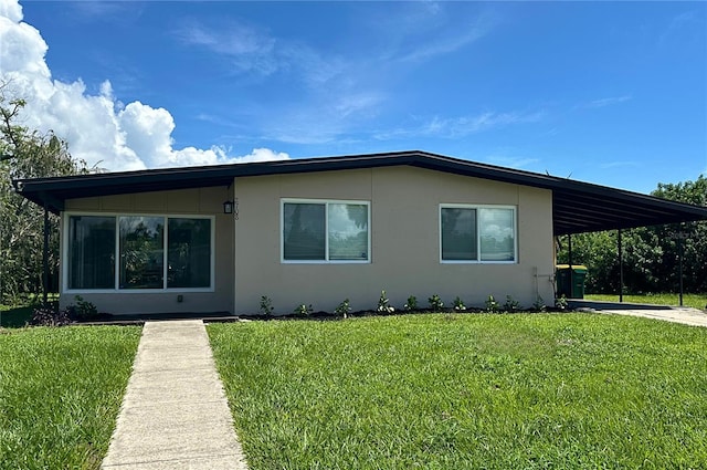 view of front of house with a carport, concrete driveway, a front lawn, and stucco siding